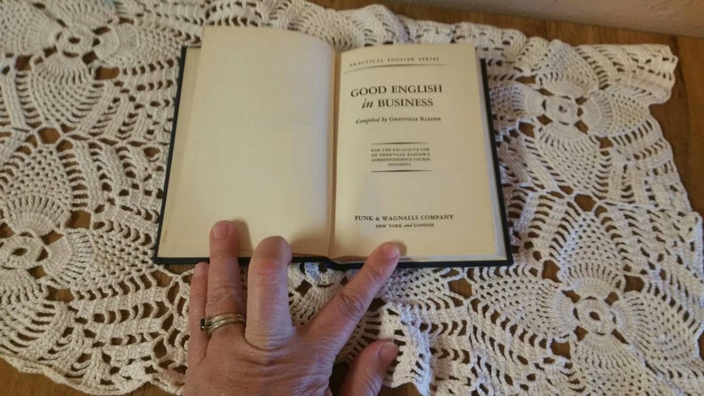 May include: A closed book titled "Good English in Business" compiled by Grenville Kleiser. The book is published by Funk & Wagnalls Company in New York and London.