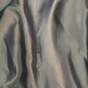 May include: Close-up of a dark gray fabric with a subtle sheen. The fabric has a vertical seam running down the center.