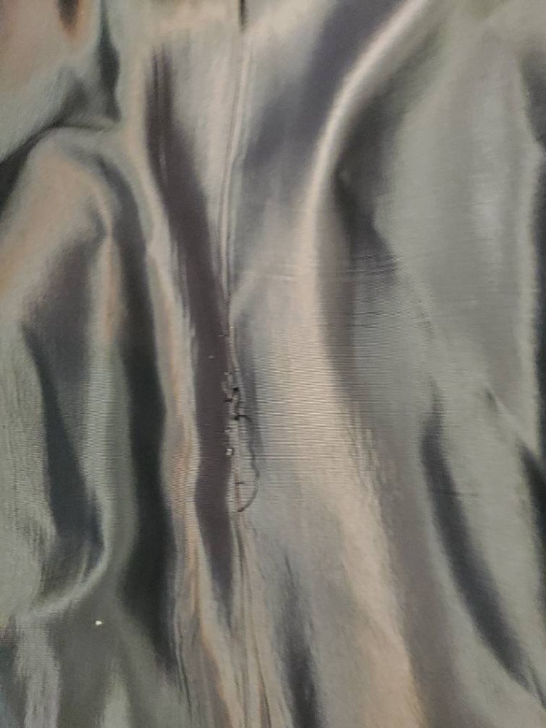 May include: Close-up of a dark gray fabric with a subtle sheen. The fabric has a vertical seam running down the center.