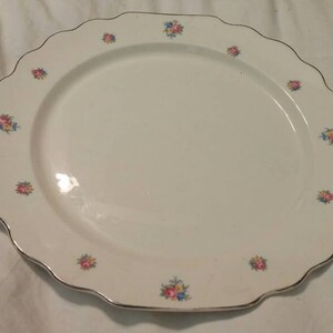 May include: White ceramic dinner plate with a scalloped edge and a floral design in pink, yellow, and blue.