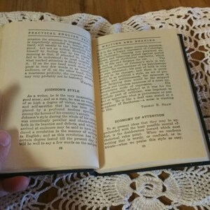 May include: An open book with a black cover and cream-colored pages. The book is titled "Practical English" and "Writing and Reading". The text on the pages discusses the writing styles of Samuel Johnson and Thomas H.  Baw.