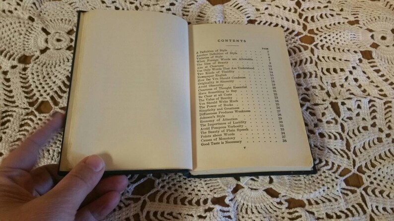 May include: An open book with a white cover and black text. The book's contents page lists topics such as "A Definition of Style", "The Value of Words", "Economy of Attention", and "Good Taste in Summary".