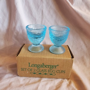 May include: A set of two blue glass egg cups in their original box. The box is brown with green text that reads "Longaberger. Set of 2 Glass Egg Cups".