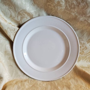 Op de afbeelding: Een wit keramisch dinerbord met een licht verhoogde rand.