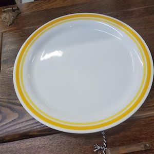 May include: White ceramic dinner plate with a double yellow band around the rim.