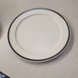 Può includere: Un piatto da portata in ceramica bianca con un bordo marrone scuro.