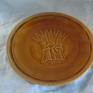 May include: A brown ceramic plate with a raised design of wheat stalks tied together. The plate has a decorative rim.