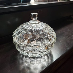 May include: A clear glass candy dish with a removable lid, featuring a textured honeycomb or diamond-cut pattern across the exterior surface. The container has a rounded, bowl-like shape and includes a small, smooth, knob-style handle on top.