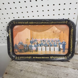 May include: A black metal serving tray with a picture of a band called "The Champagne Musicmakers" in front of a stage with curtains. The tray is decorated with musical notes and a champagne glass.