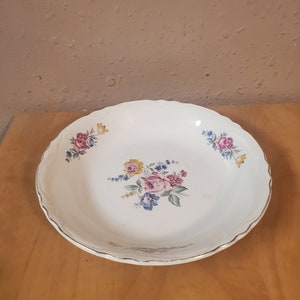 Puede incluir: Tazón de cerámica blanca con borde dorado y diseño floral. Las flores son rosas, amarillas, azules y verdes.