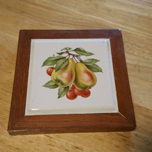 Pode incluir: Um azulejo de cerâmica emoldurado em madeira com uma imagem pintada de duas peras e cerejas vermelhas em um galho.
