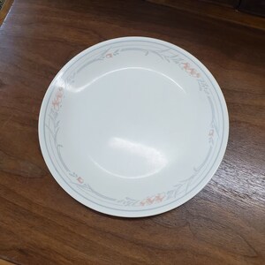 May include: A white ceramic dinner plate with a blue and grey floral design. The flowers are a light pink colour.