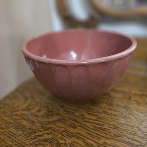May include: A dusty rose-colored ceramic bowl featuring a smooth interior and a series of vertical, rounded indentations or fluted detailing around the exterior circumference, creating a textured appearance along the side of the round vessel.