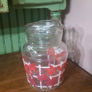 May include: A clear glass pitcher with a red and white floral design. The pitcher has a lid and is perfect for serving beverages.