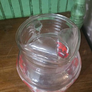 May include: A clear glass pitcher with a red and white geometric pattern. The pitcher has a lid with a handle.