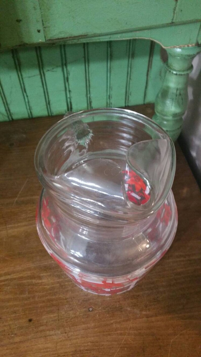 May include: A clear glass pitcher with a red and white geometric pattern. The pitcher has a lid with a handle.