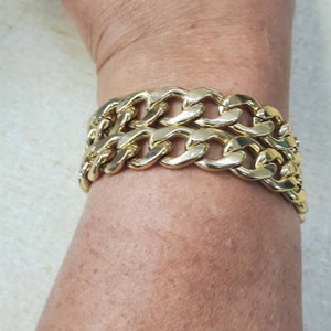 May include: A gold-colored chain link bracelet. The bracelet is made of multiple interlocking links, creating a bold and chunky design. The links are rounded and polished, reflecting light. The bracelet is worn on the wrist.
