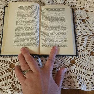 May include: An open book with the title "Practical English" and "Good English in Business" on a white crocheted doily. The book is open to a page with text about the importance of good English.
