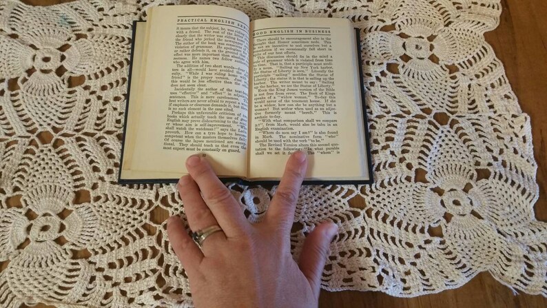 May include: An open book with the title "Practical English" and "Good English in Business" on a white crocheted doily. The book is open to a page with text about the importance of good English.