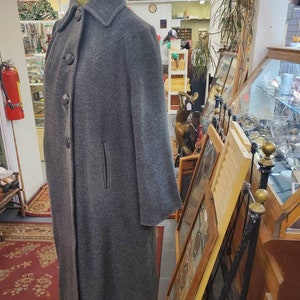 May include: A gray wool coat with a button closure and a single pocket on the left side. The coat is long and has a classic style.