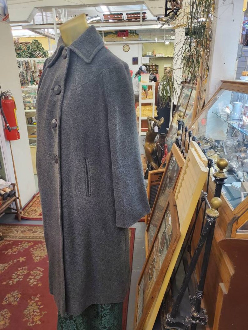 May include: A gray wool coat with a button closure and a single pocket on the left side. The coat is long and has a classic style.