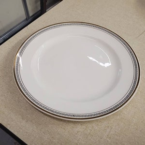Könnte beinhalten: Weißer Keramik-Dinnerteller mit gold-schwarzem geometrischem Rand.