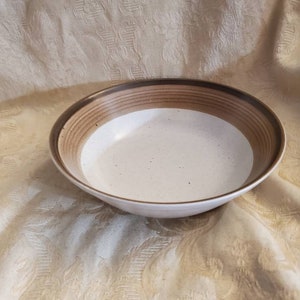 May include: A white ceramic bowl with brown stripes around the rim. The bowl has a speckled glaze.
