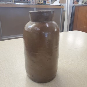 May include: A brown ceramic jar with a rounded shape and a smooth, slightly textured surface.