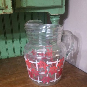 May include: A clear glass pitcher with a red and white floral design. The pitcher has a handle and a spout.