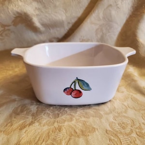 May include: White ceramic baking dish with a cherry design. The dish has two handles on the sides.