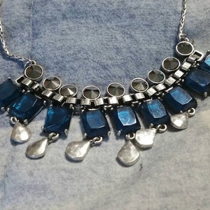 May include: A silver necklace with a row of dark blue rectangular stones and smaller silver teardrop-shaped stones hanging below.