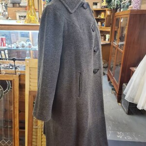May include: A long gray wool coat with a black collar and buttons. The coat has a single pocket on the left side.