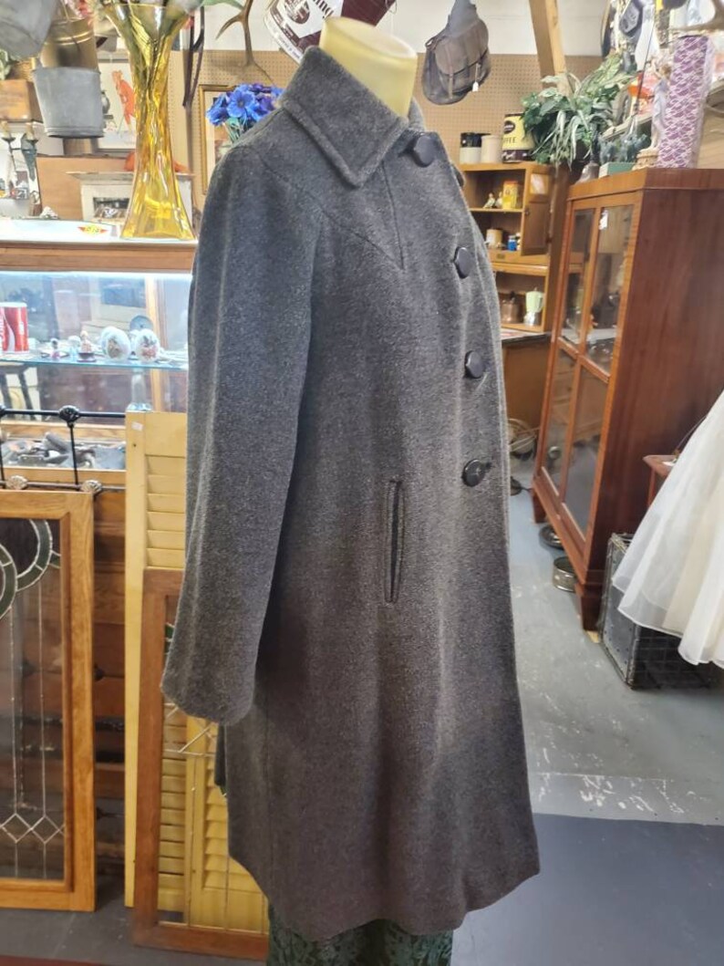 May include: A long gray wool coat with a black collar and buttons. The coat has a single pocket on the left side.