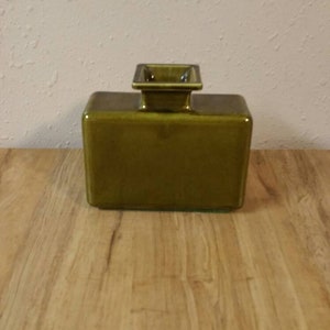 以下が含まれることがあります： 上面がわずかに盛り上がった正方形の開口部を持つ、正方形のオリーブグリーンのセラミック花瓶です。