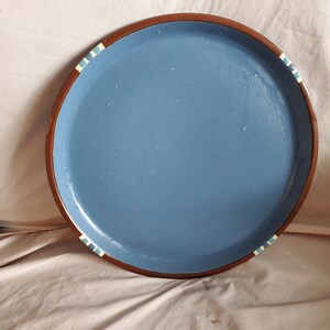 以下が含まれることがあります： 縁が茶色で、白と青のストライプが縁取りされた青いセラミック製のサービングトレイです。