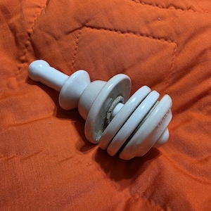 May include: White ceramic insulator with multiple stacked rings. The insulator has a rounded top and a pointed bottom.
