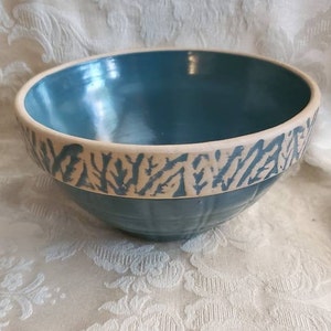 May include: A teal blue ceramic mixing bowl with a white rim and a white floral design around the top.