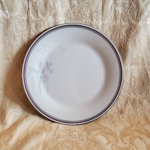 May include: A white ceramic dinner plate with a gray and burgundy rim. The plate has a floral design with a light blue and pink flower.