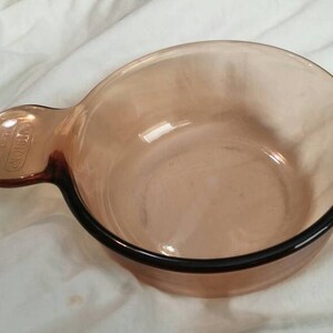 May include: A brown glass baking dish with a single handle. The dish is made of Pyrex and is designed for use in the oven.