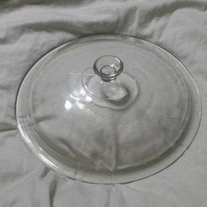 Op de afbeelding: Een glazen taartplateau met een ronde basis en een koepelvormig deksel. Het deksel heeft een klein knopje bovenop.