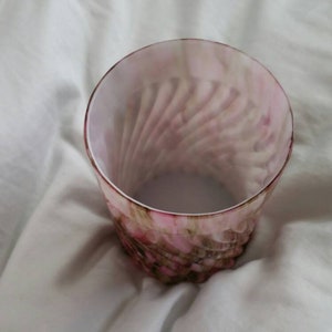 May include: A clear glass tumbler with a pink and brown swirl pattern. The glass has a rounded bottom and a straight, wide mouth.