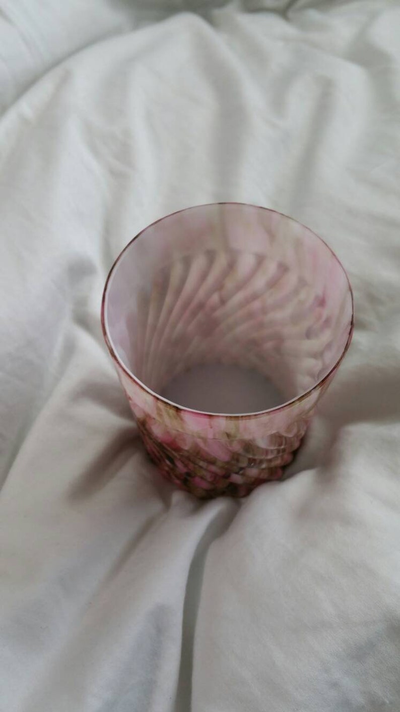 May include: A clear glass tumbler with a pink and brown swirl pattern. The glass has a rounded bottom and a straight, wide mouth.