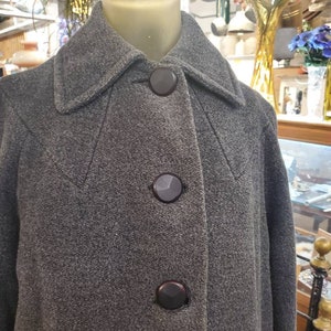 May include: A gray wool coat with a high collar and three black buttons. The coat is on a mannequin.