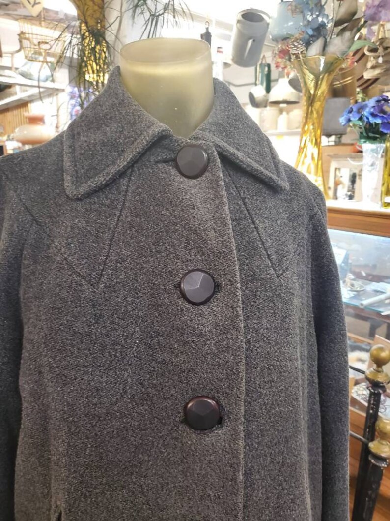 May include: A gray wool coat with a high collar and three black buttons. The coat is on a mannequin.