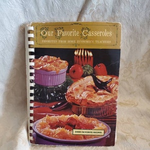 May include: A vintage cookbook titled "Our Favorite Casseroles" with a gold border and the text "Favorites from Home Economics Teachers" and "2000 Favorite Recipes". The cover features a photo of three casseroles with a red, white, and green background.