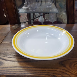 May include: A white ceramic bowl with a yellow rim. The bowl has two yellow stripes around the rim.