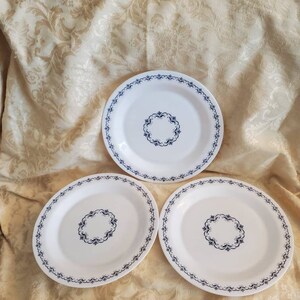 May include: Three white ceramic plates with a blue and white floral design. The plates have a scalloped edge and a simple floral pattern in the center.