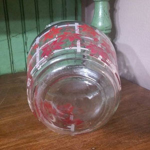 May include: A clear glass jar with a red and white floral pattern. The jar has a wide mouth and a flat bottom.