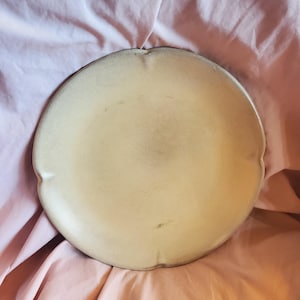 May include: A large, round, cream-colored ceramic serving platter with a slightly scalloped edge.