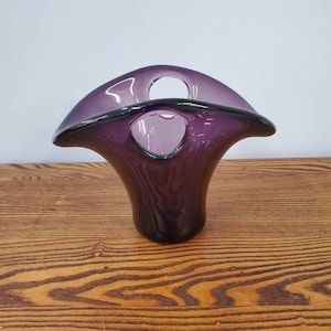 Könnte beinhalten: Eine violette Glasvase mit einem einzigartigen, offenen Design. Die Vase hat eine breite, ausgestellte Öffnung und einen schmalen Boden.